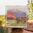 Person holding a framed artwork of a Pikes Peak in Colorado in a natural setting