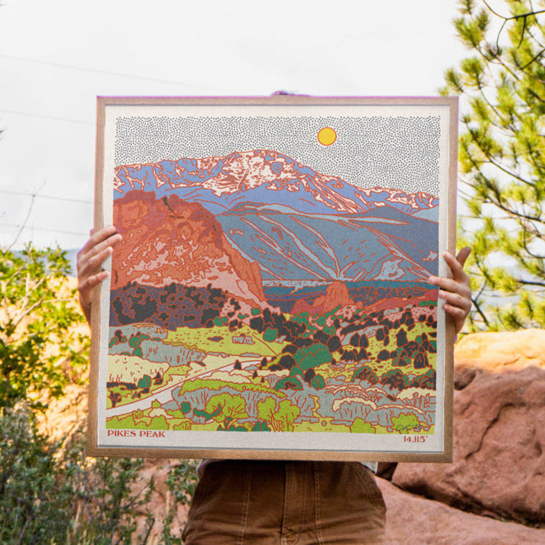 Person holding a framed artwork of a Pikes Peak in Colorado in a natural setting