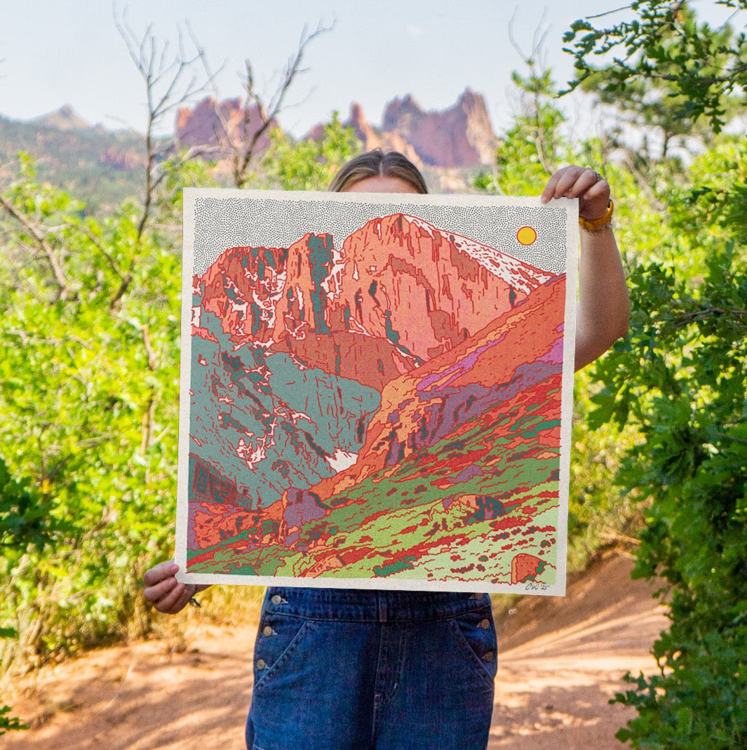 Person holding a painting of a scenic landscape with Longs Peak in Colorado in a natural setting.