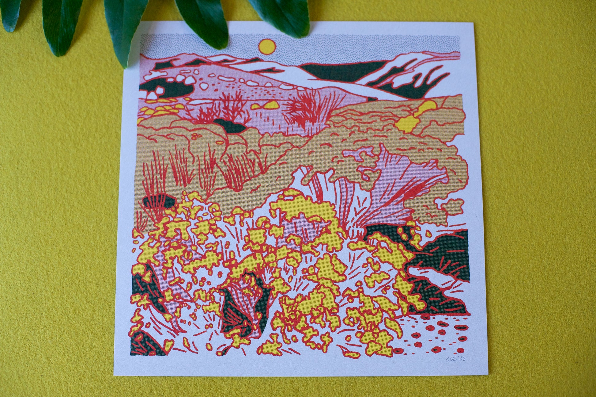 Physical print shown on top of a chartreuse felt fabric. There is a green plant leaf at the top of the frame overlapping the top of the print.