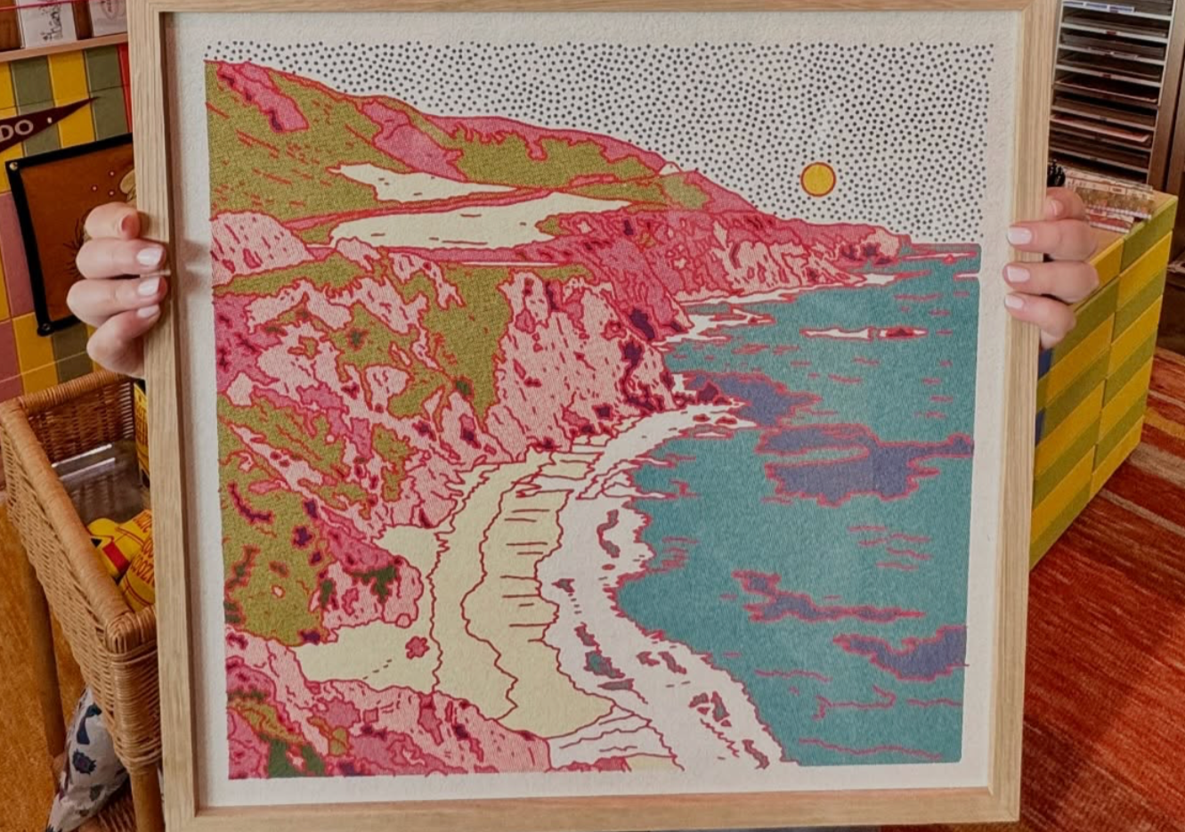 Person holding a framed vintage artwork of a Pacific Northwest coast landscape in a store setting