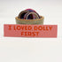 Rectangular 5” by 1.25” pink vinyl sticker with red block “I Loved Dolly First” text. The sticker is leaning against a ceramic cup filled with washi tape and a button pin.